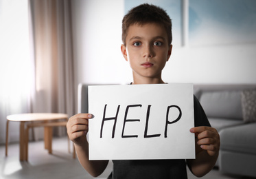 Abused little boy with sign HELP indoors. Domestic violence concept