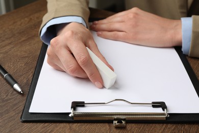 Photo of Woman erasing something on paper at wooden table, closeup