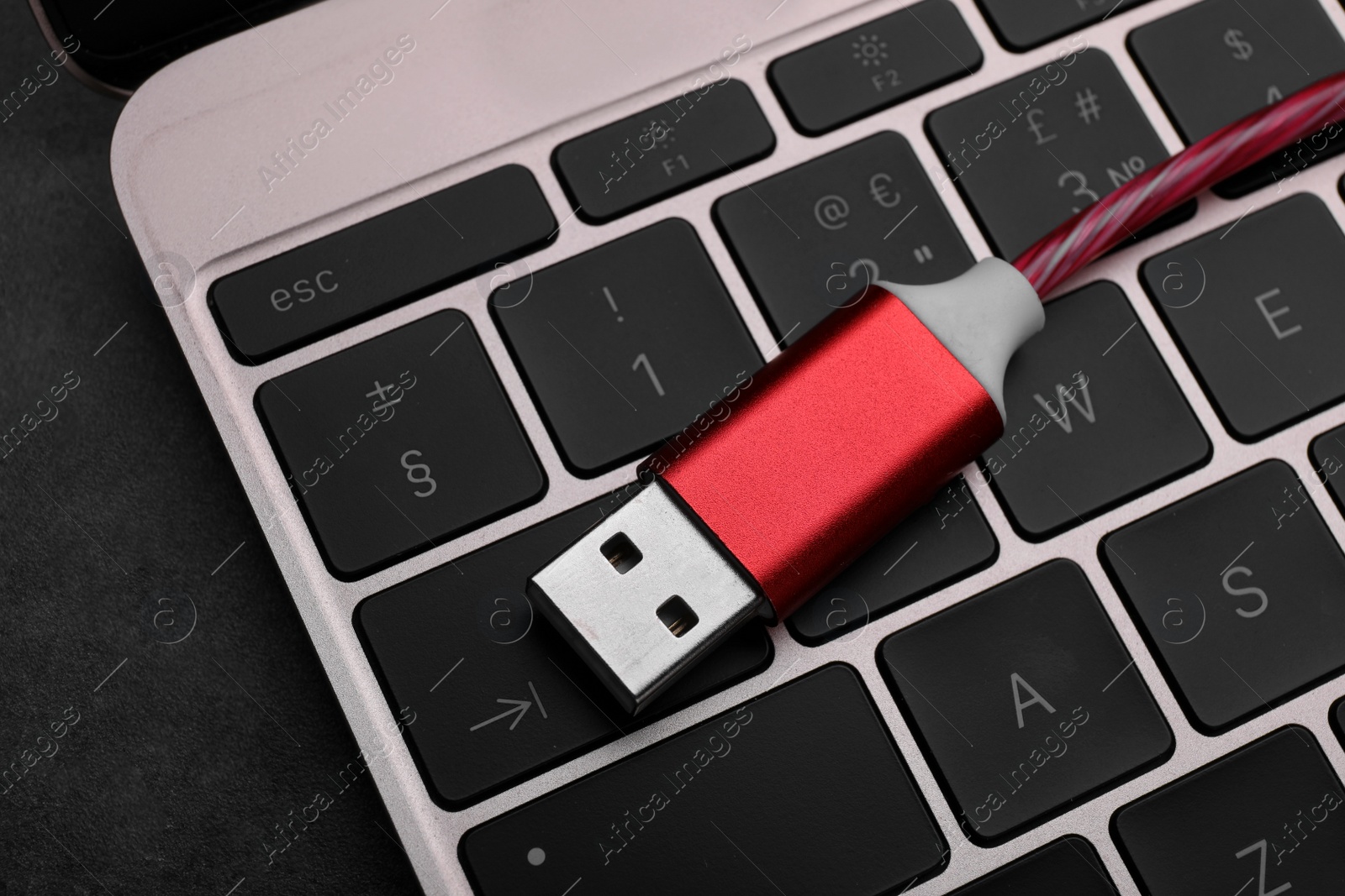 Photo of Red USB cable and laptop on dark table, closeup