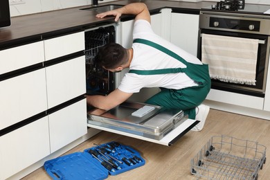 Serviceman repairing dishwasher near toolbox in kitchen