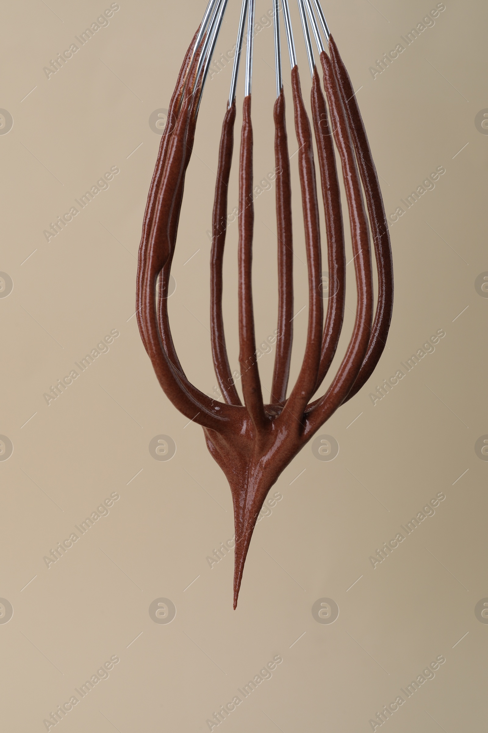 Photo of Chocolate cream flowing from whisk on beige background, closeup