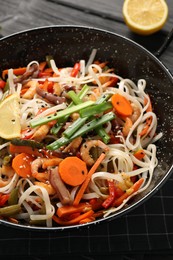 Photo of Shrimp stir fry with noodles and vegetables in wok on black wooden table, closeup
