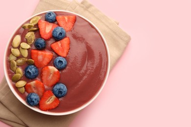 Photo of Bowl of delicious smoothie with fresh blueberries, strawberries and pumpkin seeds on pale pink background, top view. Space for text