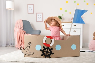 Cute little girl playing with cardboard ship at home