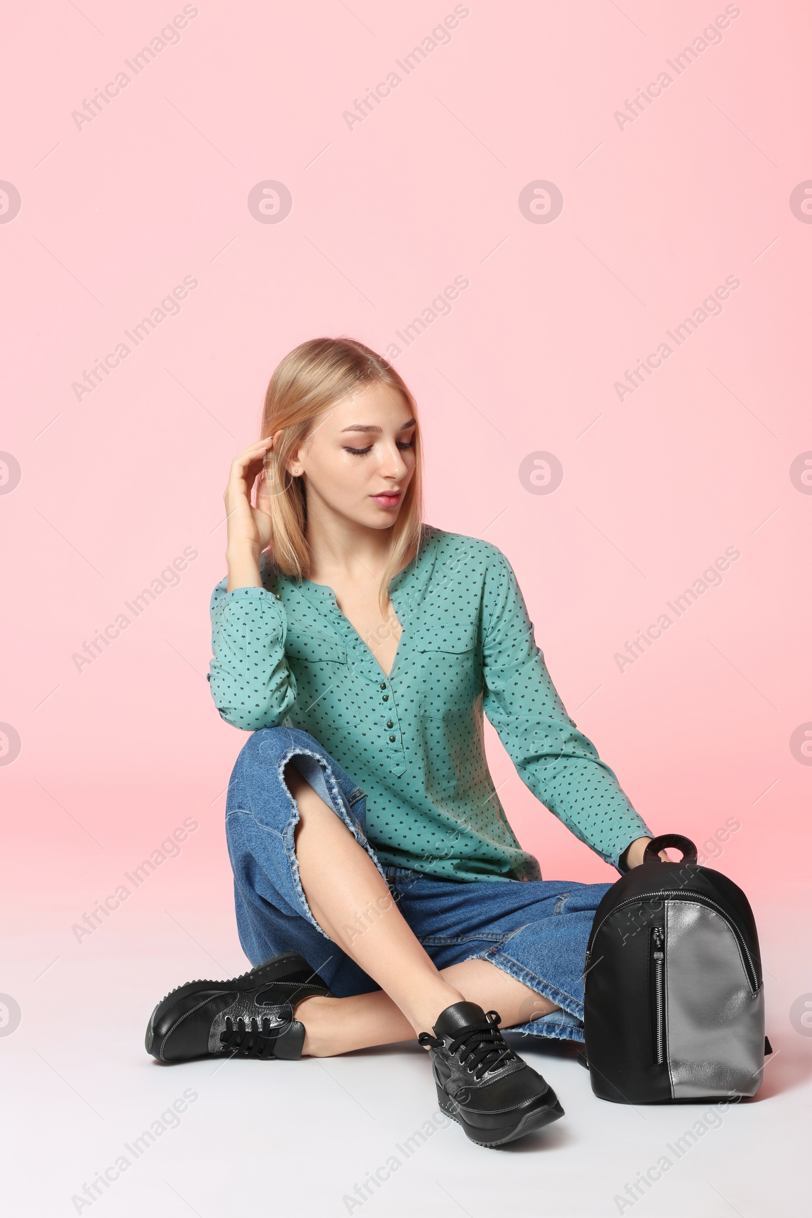 Photo of Fashionable young woman in stylish shoes with backpack sitting on color background