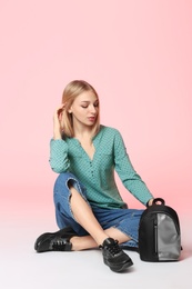 Photo of Fashionable young woman in stylish shoes with backpack sitting on color background