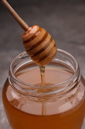 Photo of Pouring sweet golden honey from dipper into jar at table, closeup