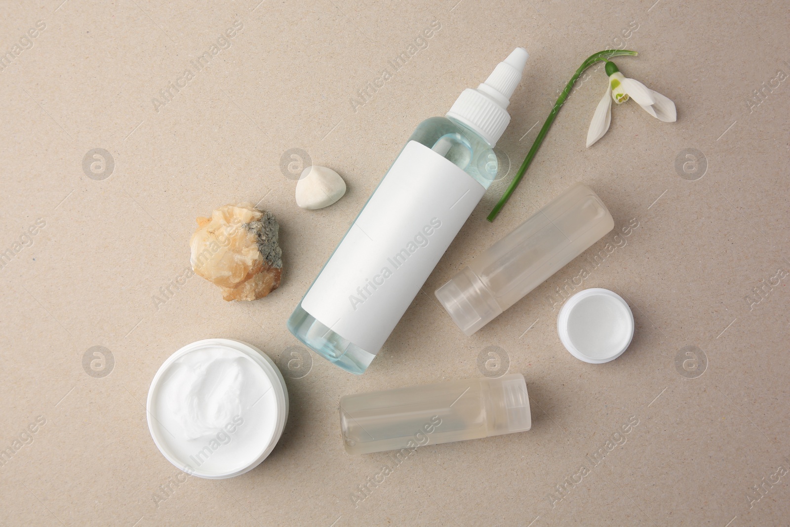 Photo of Different cosmetic products, stones and snowdrop flower on beige background, flat lay