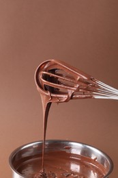 Chocolate cream flowing from whisk into bowl on brown background