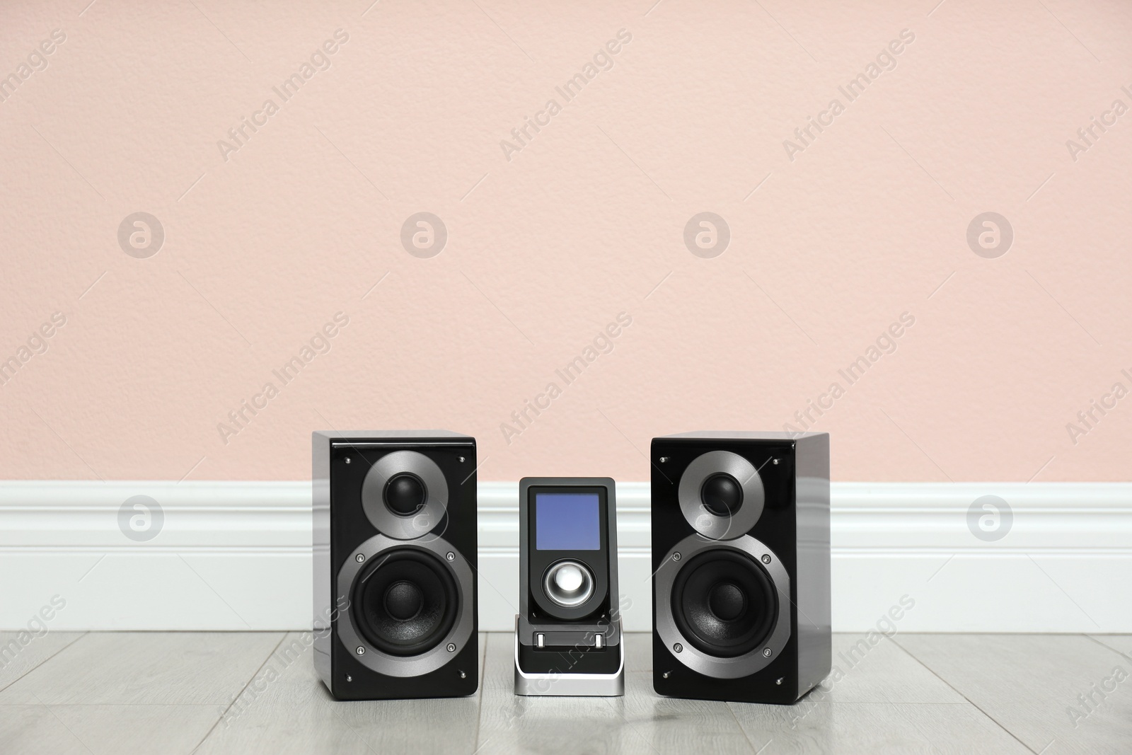 Photo of Modern powerful audio speakers and remote on floor near pink wall. Space for text