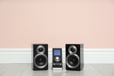 Modern powerful audio speakers and remote on floor near pink wall. Space for text