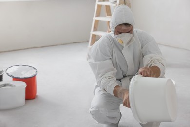 Photo of Decorator holding bucket with paint on white floor in room