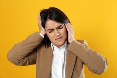 Young woman suffering from migraine on yellow background