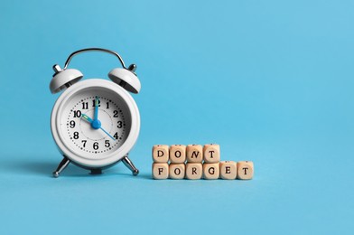 Alarm clock and cubes with phrase Don't forget on light blue background, space for text. Reminder concept