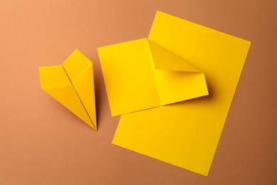 Photo of Handmade yellow plane and pieces of paper on brown background, flat lay