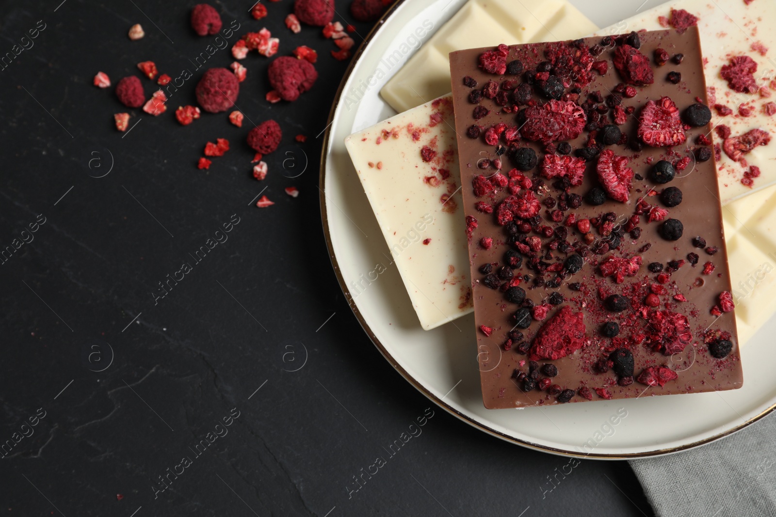 Photo of Chocolate bars with freeze dried fruits on black table, flat lay. Space for text