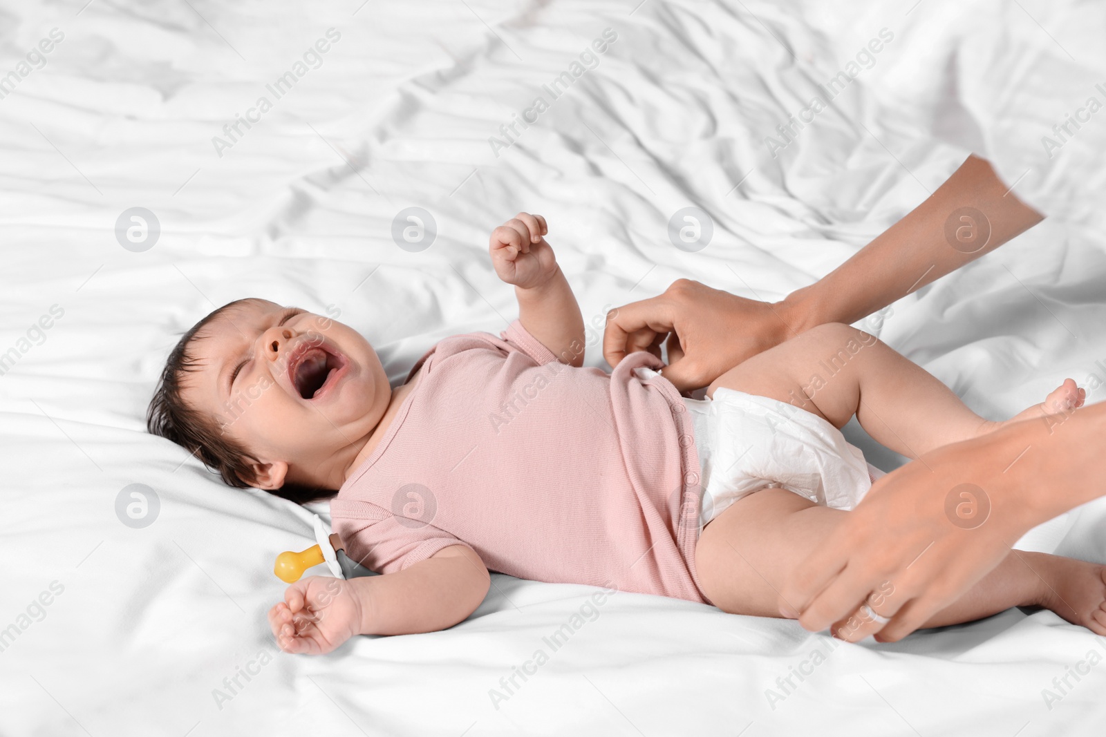 Photo of Mother putting clothes on crying daughter on bed, closeup