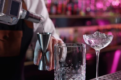 Photo of Cocktail making. Bartender pouring alcohol from bottle into jigger at counter in bar, closeup