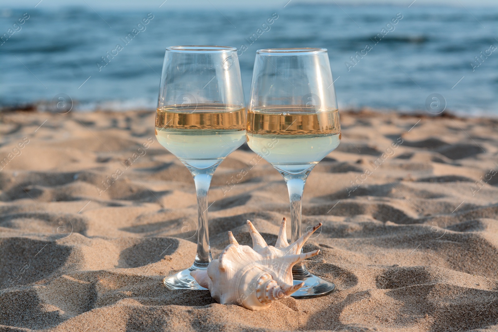 Photo of Glasses of tasty wine and seashell on sand near sea