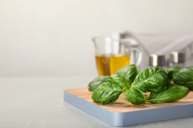 Photo of Wooden board with fresh green basil leaves on table. Space for text