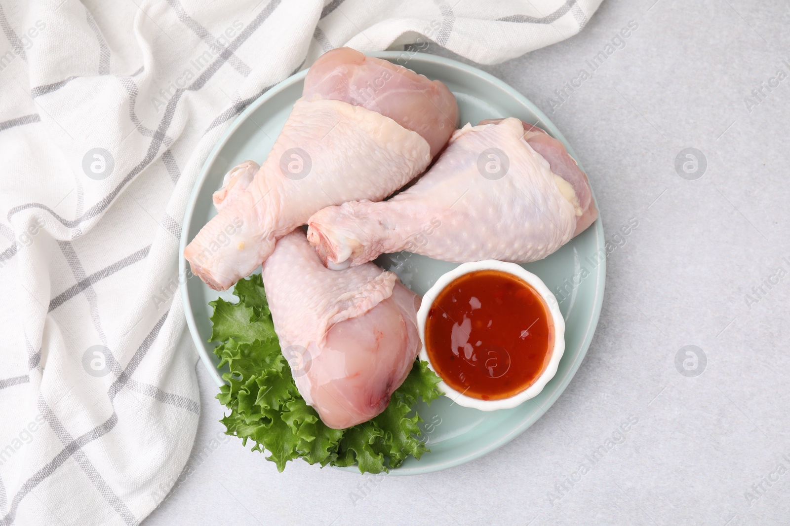 Photo of Fresh marinade, raw chicken drumsticks and lettuce on light table, top view