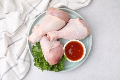 Fresh marinade, raw chicken drumsticks and lettuce on light table, top view