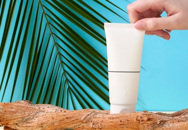 Woman with tube of cream and plant against light blue background, closeup