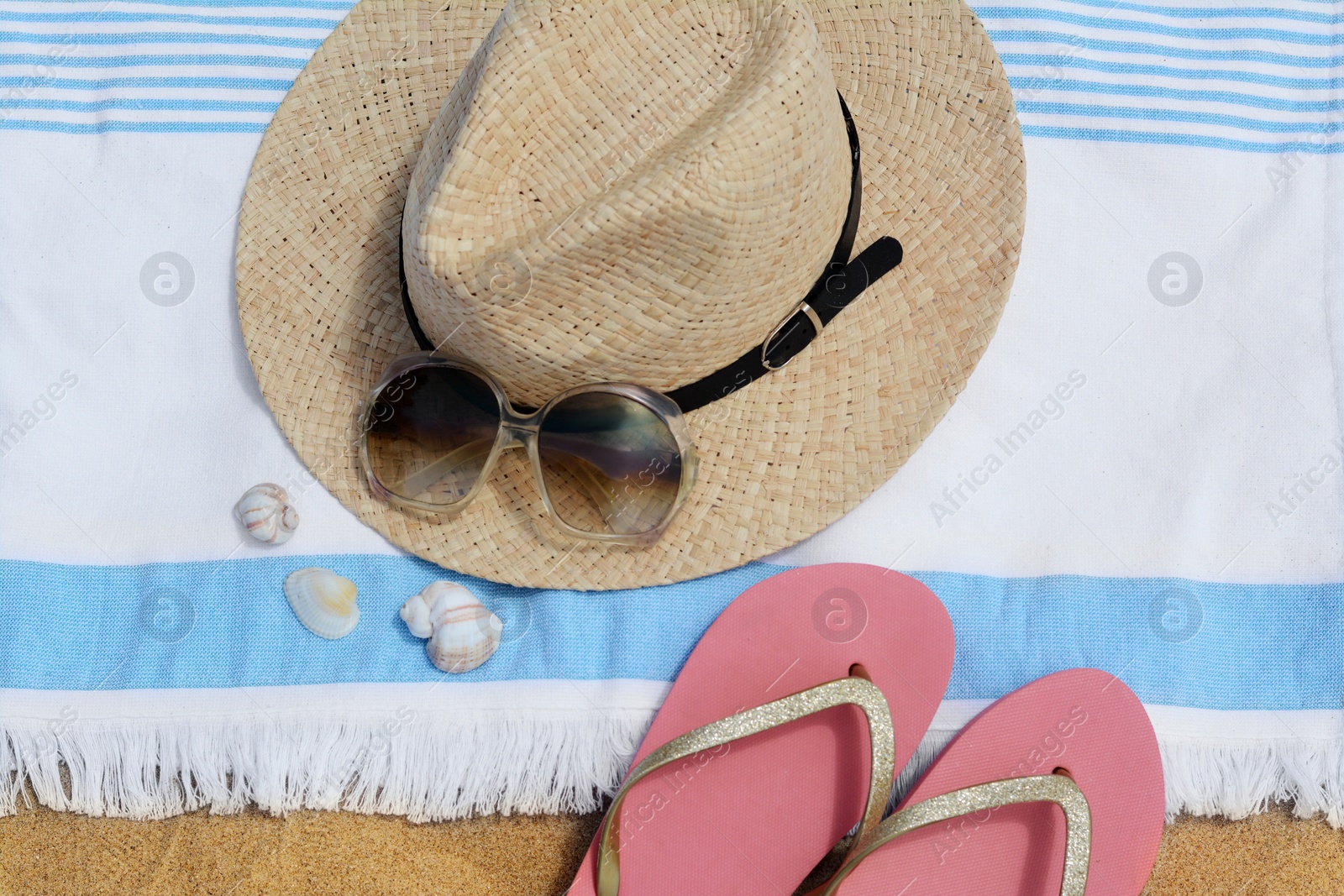 Photo of Beach towel with straw hat, seashells, sunglasses and flip flops on sand, flat lay