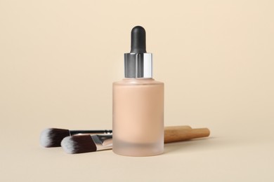 Bottle of skin foundation and brushes on beige background. Makeup product