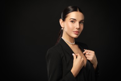 Young woman with elegant pearl jewelry on black background, space for text