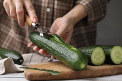 Photo of Woman peeling fresh cucumber at white wooden table, closeup