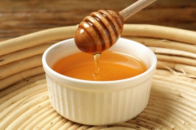 Pouring tasty honey from dipper into bowl on table, closeup