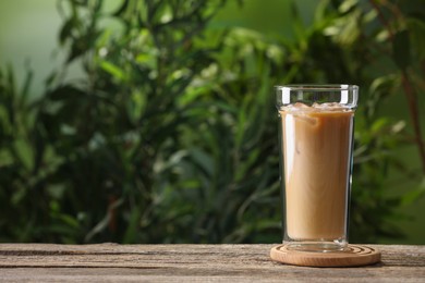 Photo of Glass of iced coffee on wooden table outdoors. Space for text