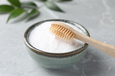 Photo of Bamboo toothbrush and bowl of baking soda on light gray marble table, closeup