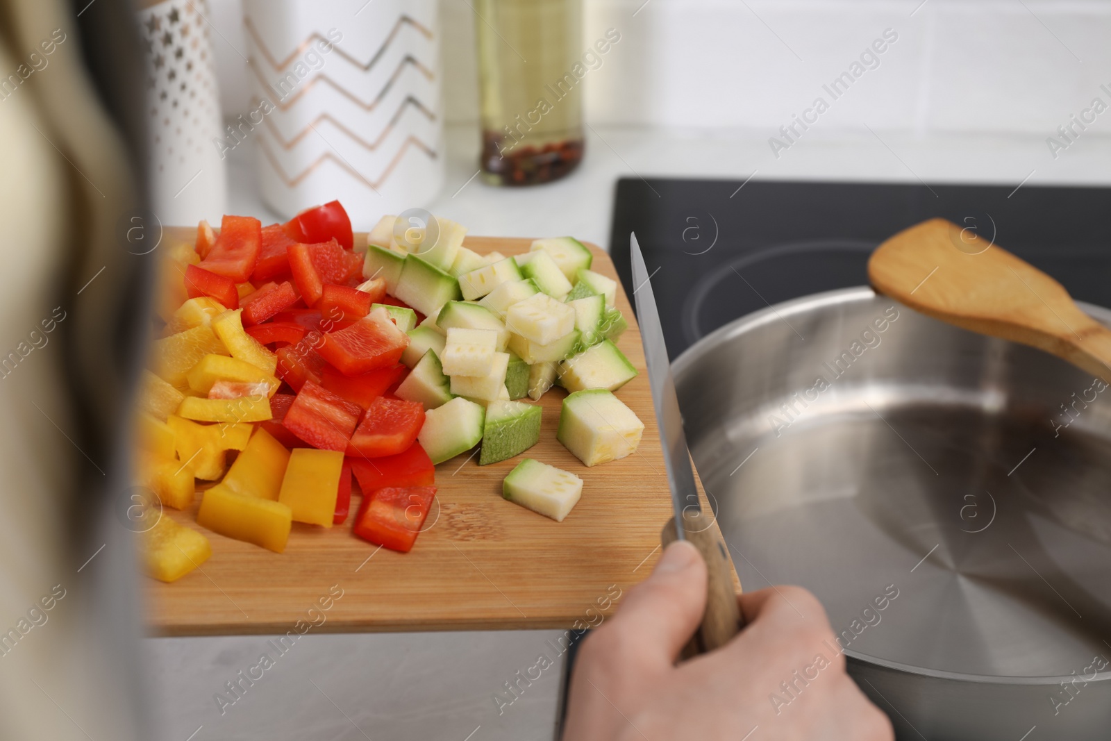 Photo of Woman putting cut vegetables into saute pan in kitchen, closeup