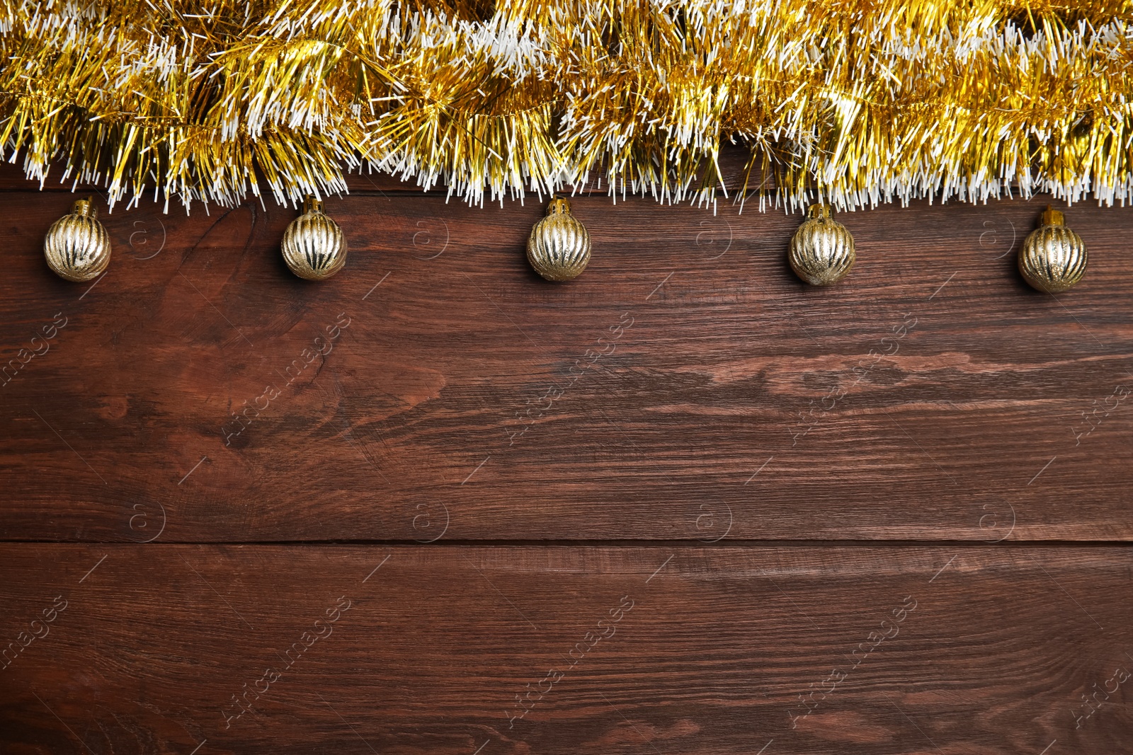 Photo of Golden tinsel and Christmas balls on wooden background, flat lay. Space for text