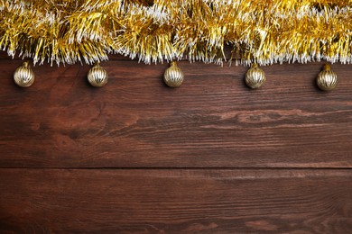 Golden tinsel and Christmas balls on wooden background, flat lay. Space for text