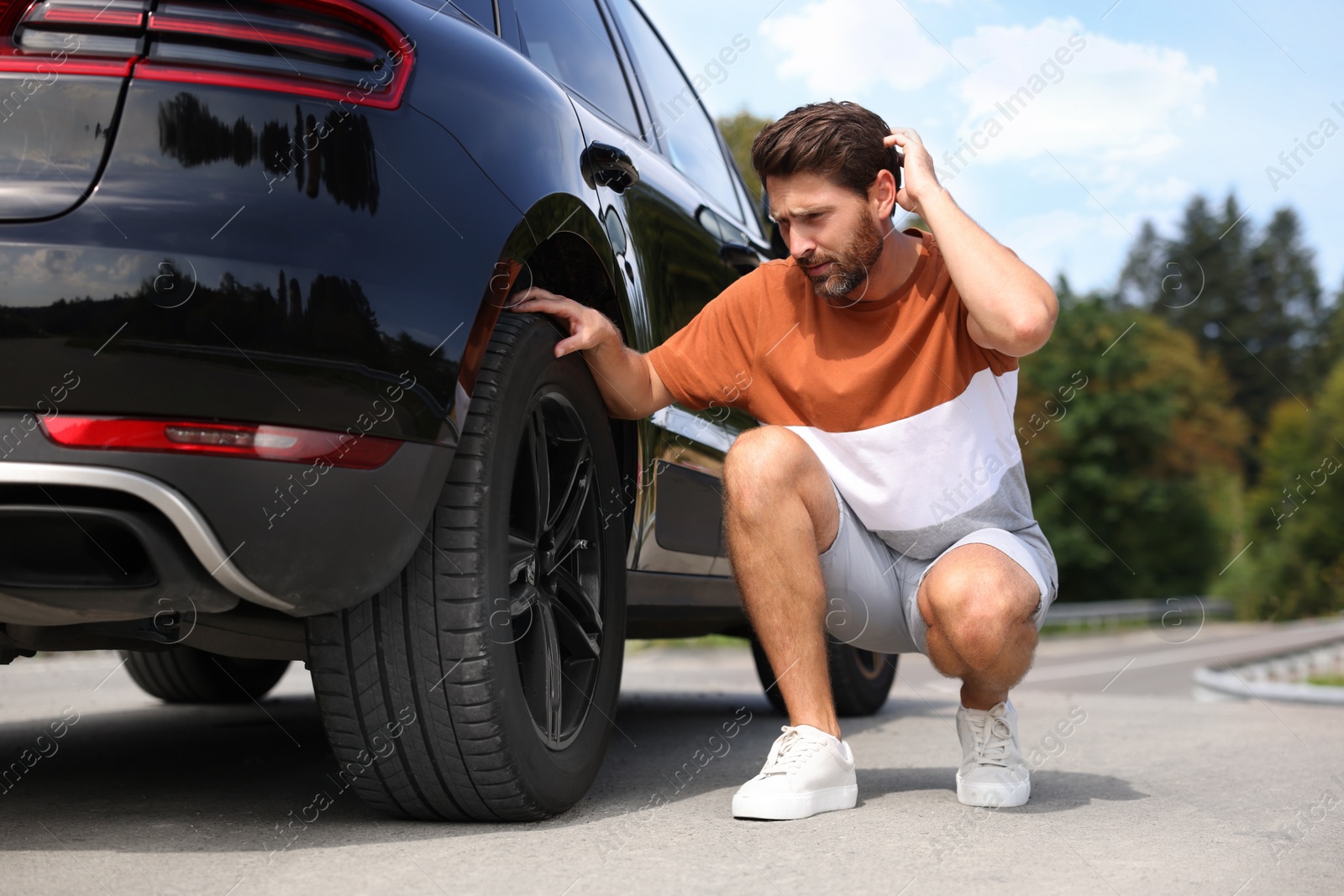 Photo of Tire puncture. Man checking wheel of car on roadside outdoors