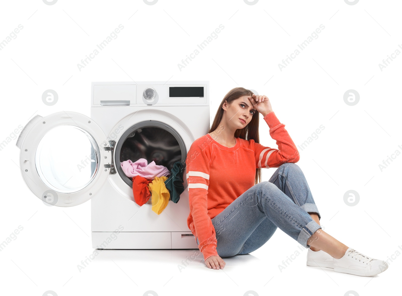 Photo of Young woman sitting near washing machine with dirty laundry on white background