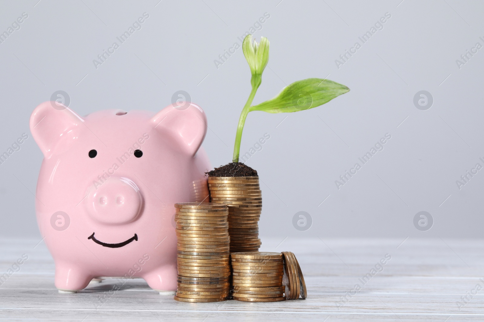 Photo of Stacks of coins with flower and piggy bank on white wooden table, space for text. Investment concept