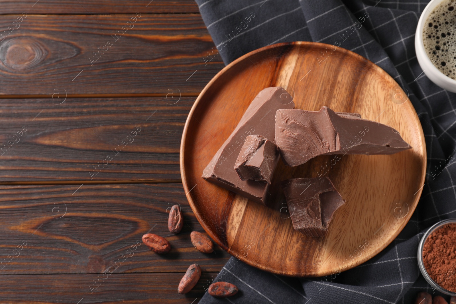 Photo of Pieces of tasty milk chocolate, cocoa beans and powder on wooden table, flat lay. Space for text