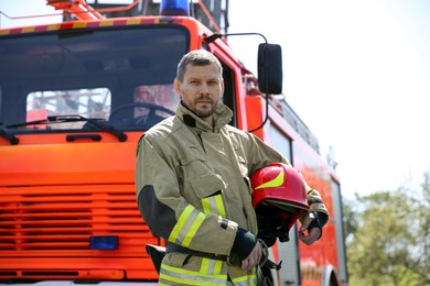 Photo of Portrait of firefighter in uniform with helmet near fire truck outdoors