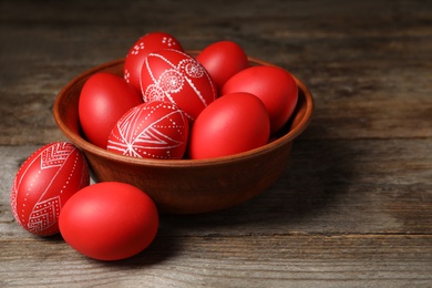 Photo of Wooden bowl with red painted Easter eggs on table. Space for text