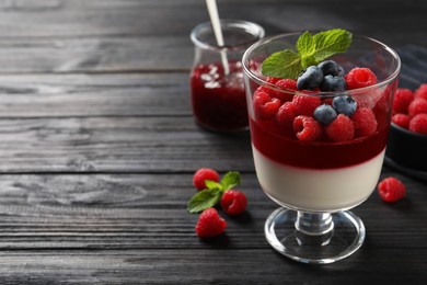 Photo of Delicious panna cotta with berries on black wooden table. Space for text