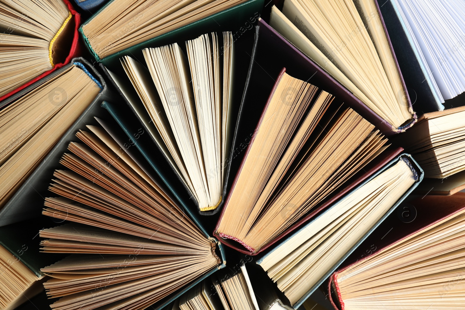 Photo of Many different hardcover books on dark background, top view