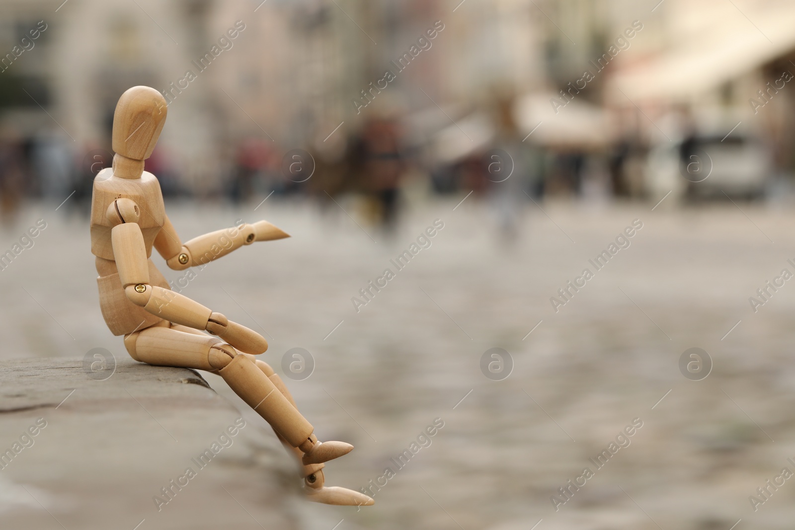 Photo of Wooden human figure sitting on curb outdoors, space for text