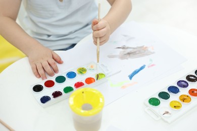 Little boy painting with brush and watercolor at white table, closeup
