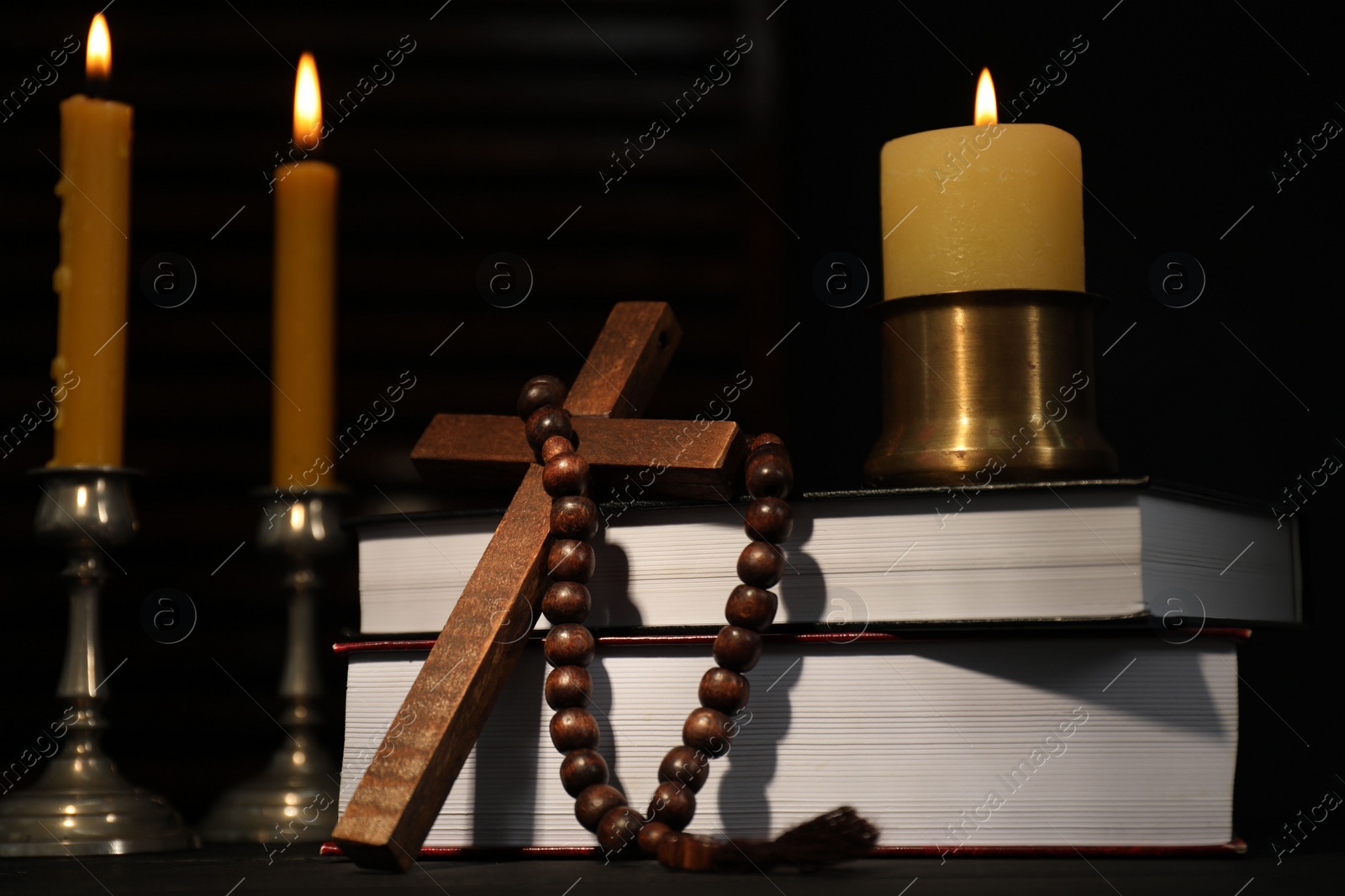 Photo of Church candles, Bible, rosary beads and cross on table in darkness