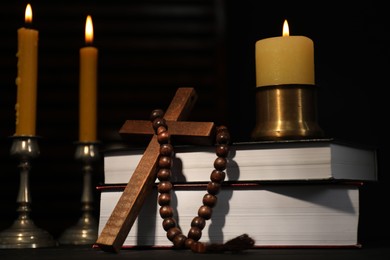 Photo of Church candles, Bible, rosary beads and cross on table in darkness