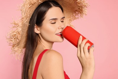 Photo of Beautiful young woman with straw hat drinking from tin can on pink background
